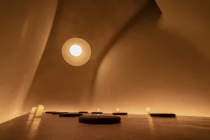A minimalist, concrete-walled room with a circular skylight and lit candles arranged on the floor.