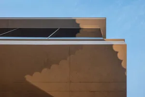 Modern building facade with concrete walls and geometric windows against a blue sky.