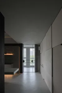 An industrial-style corridor with concrete walls and floor, featuring a sleek, minimalist design with a glass door at the end