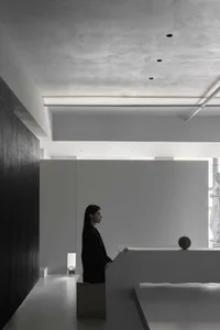 A minimalist space featuring exposed concrete walls and ceiling, with a lone figure standing in the background.