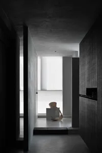 A minimalist interior space with concrete walls and floor, featuring a modern sculpture on a platform in a hallway.