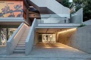 A modern office space with concrete walls and floors, featuring a staircase and glass balcony.