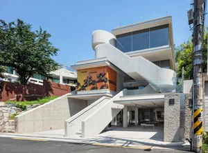 Modern residential building with white stone and concrete exterior, featuring glass windows and a sleek, contemporary design.