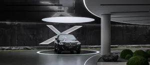 A black BMW car displayed on a circular platform in a futuristic architectural space with metallic and stone surfaces.