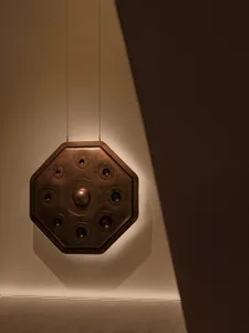 A minimalist metal decorative object with lighting features hanging in a neutral setting.