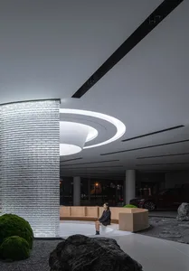 A modern lobby featuring glass walls and concrete flooring with a person sitting on a wooden bench.