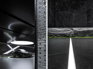 A sleek, minimalist showroom interior featuring a black vehicle displayed on a circular platform with lighting and black mate