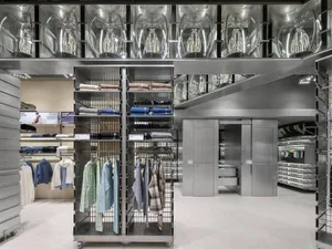商業零售店內部空間，展示金屬陳列架與服裝商品，以及玻璃天花板搭配工業燈具