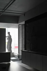 A minimalist modern kitchen featuring black marble countertops and concrete walls.