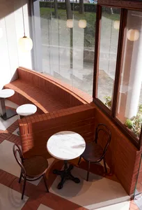 Circular marble table with vintage wood chairs, set in a cozy cafe window seat with brick walls and a view outside through la