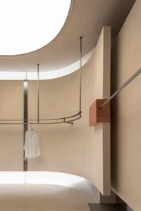A minimalist clothing display featuring a white garment on a metal rod in a curved, nude-colored space.