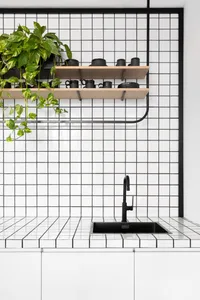 A modern minimalist kitchen with white tiled walls and black appliances and accessories.
