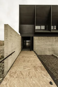 A modern, minimalist concrete exterior of a building with a stone pathway and gravel area.