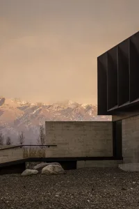 A modern building made of concrete with mountains in the background.