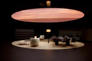 A modern conference room featuring wooden furniture, including a long oval table surrounded by armchairs and a couch.