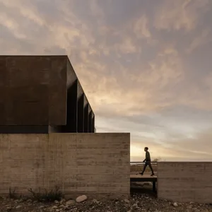 A modern building with concrete and steel exterior features a pathway with a person walking along it.