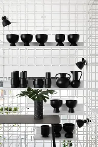 Black ceramic vessels and bowls arranged on white shelves in a minimalist interior design setting.