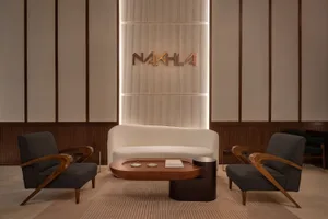 An image of a modern lobby with a white cushioned seating area, two dark gray curved armchairs, and a wooden coffee table.