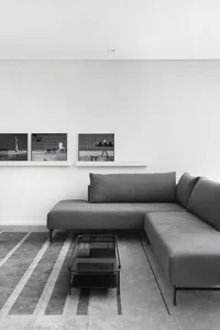 A minimalist living room featuring a gray sectional sofa on a patterned concrete floor, with a glass coffee table and framed 
