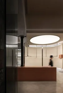 A modern office space featuring a wooden reception counter with a large circular light fixture above it and a blurred figure 