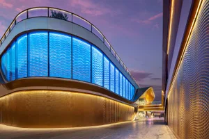 A modern retail pavilion with glass walls and blue lighting at dusk.