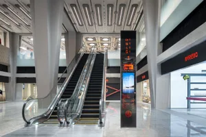 A modern shopping center with glass and concrete design, featuring escalators.