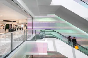 Modern shopping mall interior with glass walls and colorful flower installations.