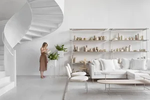 A modern minimalist living room with a spiral staircase, concrete floor, leather and wood furniture, and concrete planters.