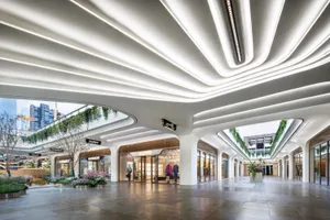 Interior of a modern shopping center with a white concrete ceiling, glass storefronts, and greenery.