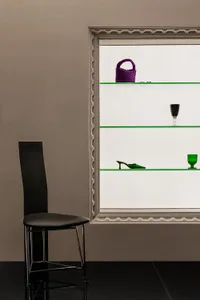 A modern glass display case showcasing a pair of green high-heeled shoes and a purple woven bag.