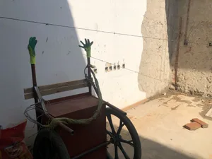 一台風化生鏽的金屬手推車，握把上放著手套，靠在有洞的白牆前。