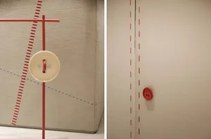 A display featuring a large beige button with a red rod and crosshatch lines drawn on a fabric surface, with a smaller red bu