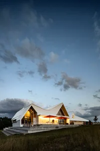 Modern commercial building with metal-clad angled roof, illuminated exterior at dusk with cloudy sky