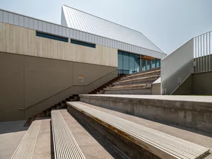 A modern architectural structure with metal roof, wooden elements, and concrete seating areas.