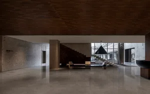 A modern office interior with concrete walls and flooring, featuring a wooden ceiling and a large black lamp.