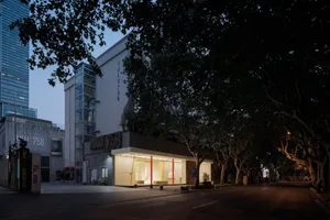 Modern street with a brightly lit storefront on the left side, featuring an illuminated entrance and large display windows.