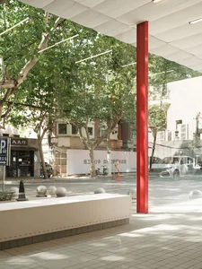 Concrete urban street with a red cylindrical column, trees, and a white canopy overhead.