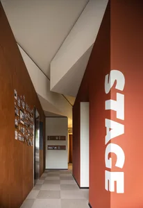 A modern office hallway with wooden walls and floors, featuring an angle view that leads to a stage area.