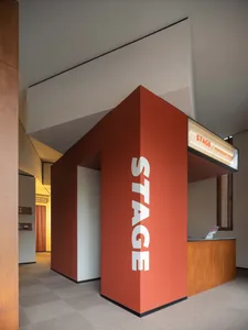 Modern interior design featuring a stage entrance with a striking red wall and a concrete column.