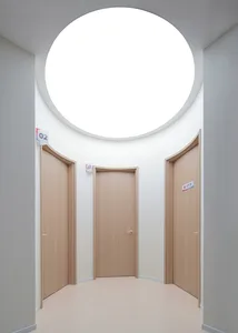 An interior view of a hospital showing three wooden doors and a round window allowing natural light.