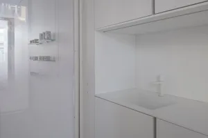 A minimalist white kitchen with white tiles, clean lines, and a white countertop.