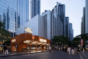 A modern, architecturally striking commercial building with a unique metal-clad façade and illuminated signage in a bustling
