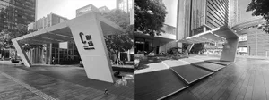 A modern, angular metal entrance structure with a geometric design, located in a cityscape with high-rise buildings and trees