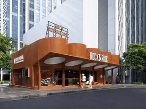A modern, industrial storefront with a rusted, corrugated-metal exterior and an open-air concept, featuring a motorcycle disp
