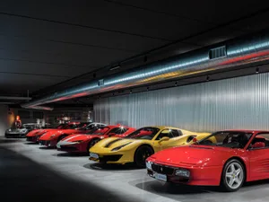 一排紅色與黃色跑車停放在金屬牆面與天花板的昏暗車庫內。