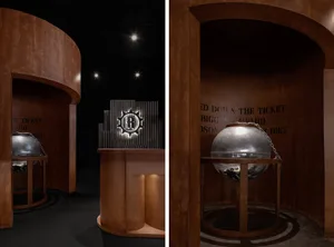 A metal sphere with a textured surface and chain links on a wooden stand in an industrial-themed exhibit environment.