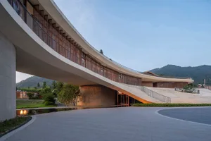 A modern architectural structure featuring concrete and glass materials, with a curved exterior and open floor plans.