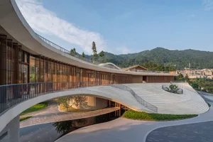 A modern pavilion constructed from concrete with a curved roof and surrounding greenery.