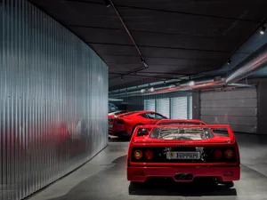 Modern automotive garage with red classic cars parked inside, metal wall on the left, concrete flooring.