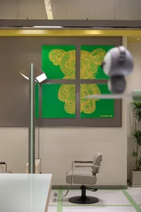 A modern hair salon interior featuring metallic furniture, green matte finish walls, and a decorative plant.